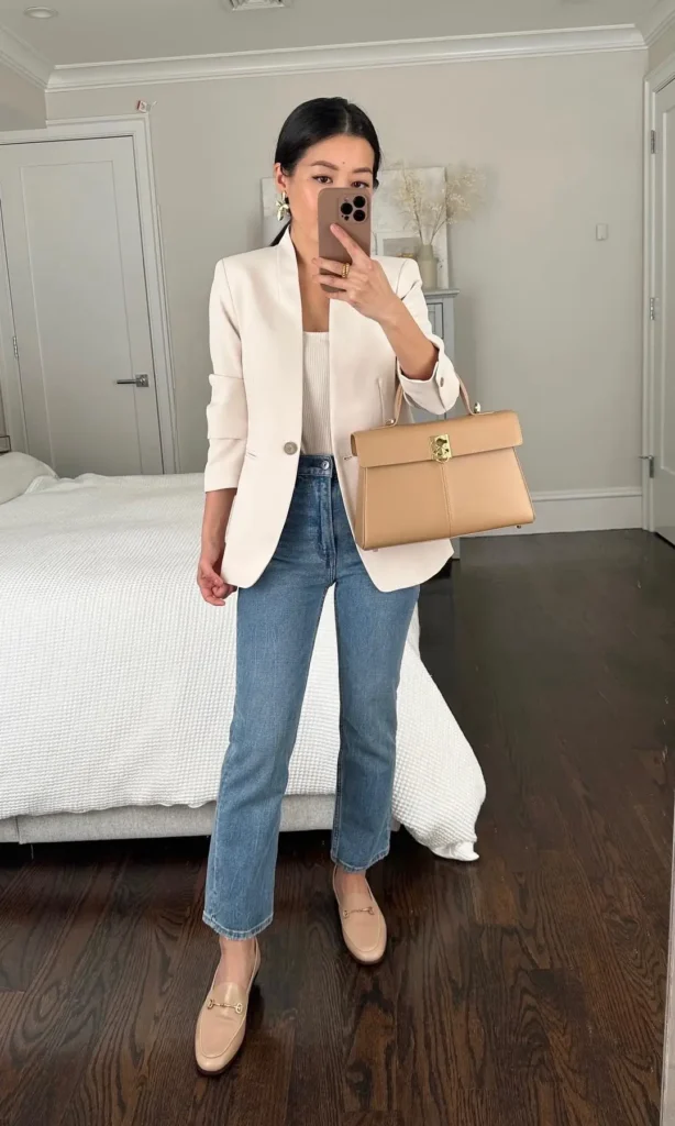 Petite woman in a cream single-button fitted blazer with light wash straight jeans, tan gold-hardware loafers, and a structured tan top-handle bag, mirror selfie