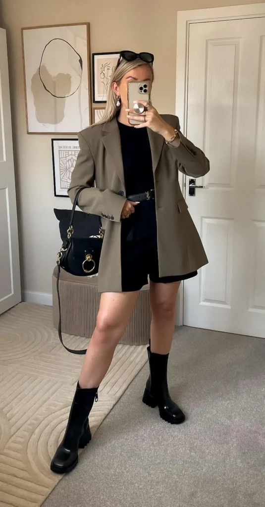 Khaki oversized blazer with a black fitted top, black shorts, chunky black knee-high boots, and a black bag with gold ring hardware, mirror selfie