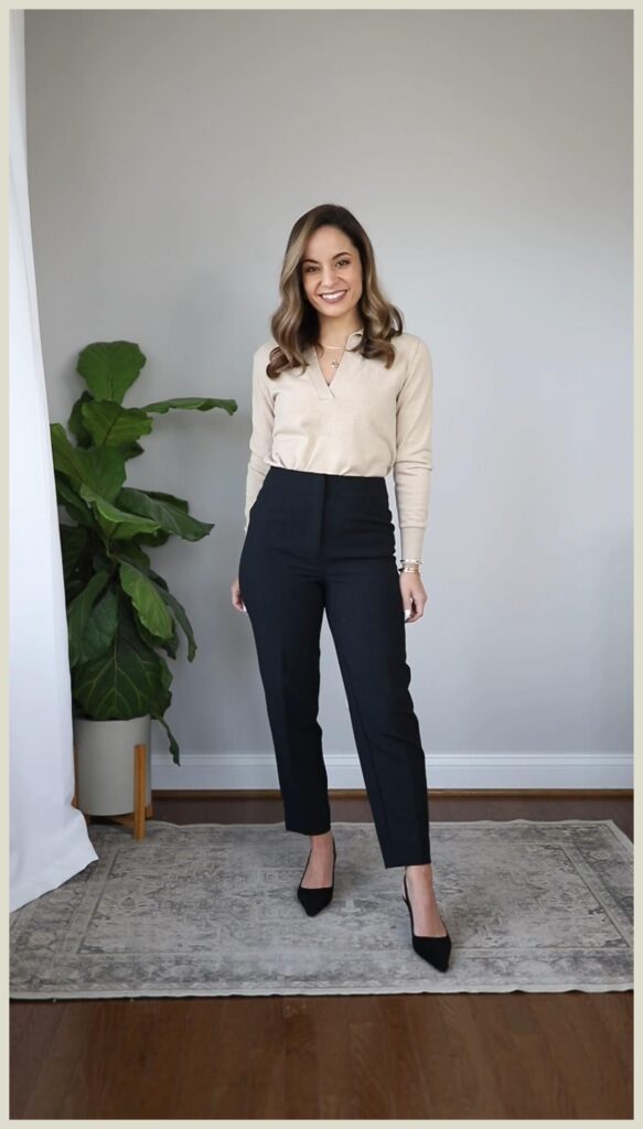 Petite woman wearing a cream oatmeal V-neck polo collar knit sweater tucked into high-waisted slim navy ankle trousers with black pointed-toe pumps and a delicate layered necklace, a minimal low maintenance petite work outfit for a polished office look