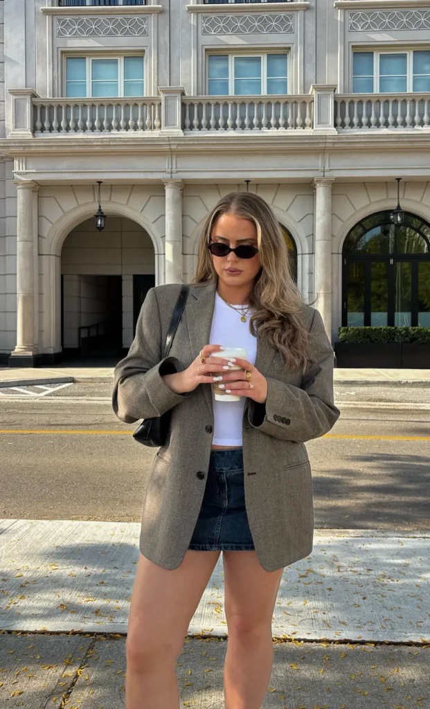 Oversized grey blazer worn over a white crop tee and denim mini skirt with a black shoulder bag, street style photo
