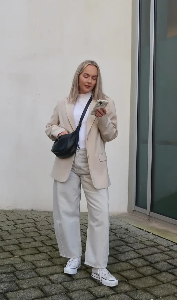 Oversized sand blazer with ecru wide-leg jeans, a ribbed white mock-neck top, white platform high-top sneakers, and a black crescent crossbody bag, street style