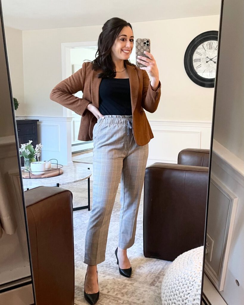 A petite woman in a soft brown blazer over a black camisole and gray glen plaid pull-on ankle trousers, finished with black pointed pumps and a gold necklace, photographed in a mirror selfie as a comfortable petite work outfit.