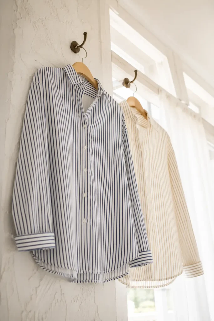 Navy and white vertical pinstripe shirt on a wooden hanger against a whitewashed wall