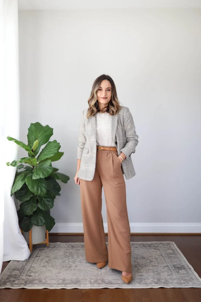 Petite woman wearing a grey plaid oversized blazer over an oatmeal ribbed knit top, high-waisted camel wide-leg trousers with a tan leather belt, and camel pointed pumps, styled as a petite casual Friday work outfit.