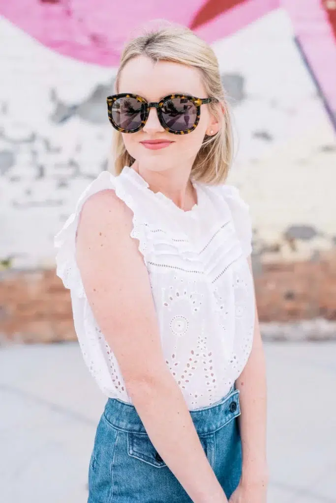 Close-up of a woman in a structured white ruffled eyelet blouse paired with high-rise wide-leg blue jeans and tortoiseshell sunglasses.