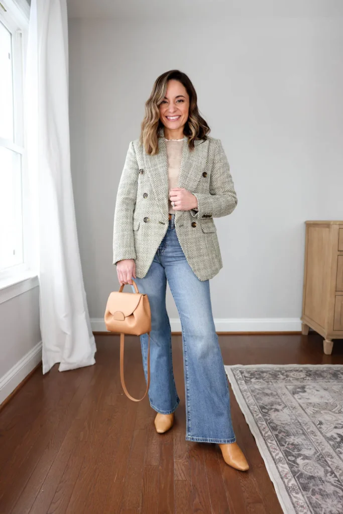 Petite woman in very light wash faded flare jeans with a raw hem, wearing a white boxy short-sleeve tee and a wide-brim structured straw hat with a decorative band, styled with a tan suede belt bag on a tooled leather strap, layered gold necklaces, and stacked bracelets.