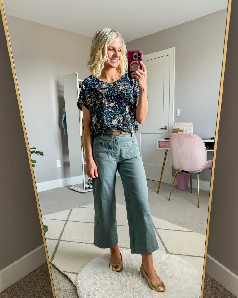 Petite woman wearing sage green high-rise wide-leg cropped pants with a tucked-in navy floral top, tan belt, and gold ballet flats showing how to pick shoes with a pointed toe or low profile for wide-leg pants