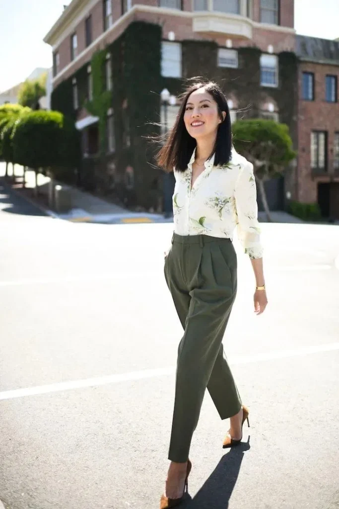 A petite woman in a cream button-up blouse with a small-scale botanical print tucked into olive high-waisted pleated trousers, showing how a delicate, well-spaced pattern sits proportionally on a petite frame without overwhelming it.