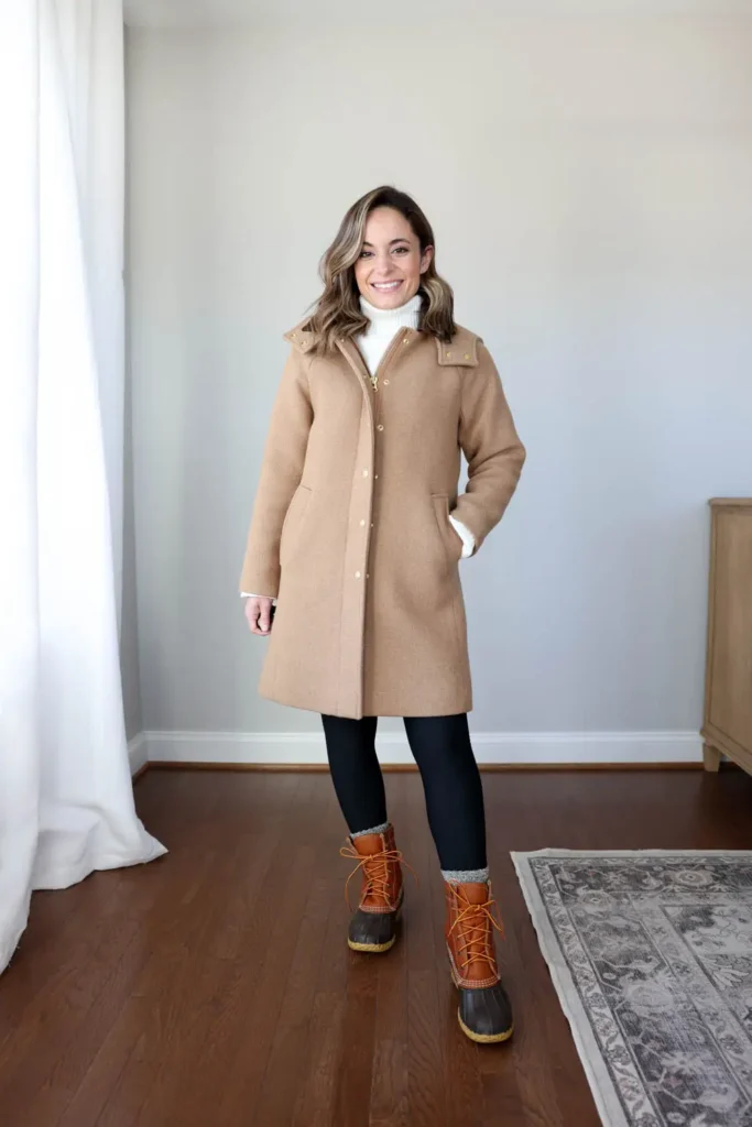 Camel Coat, Turtleneck and Duck Boots, petite woman in knee-length camel wool coat, dark slim leggings and cognac duck boots with marled socks indoors.