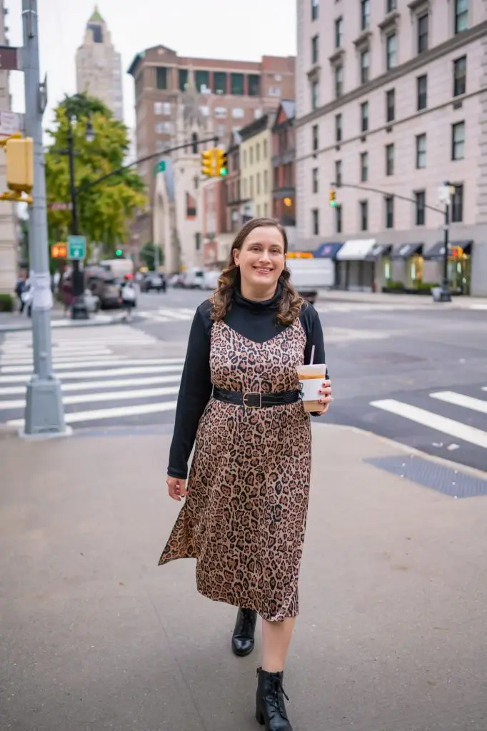 Leopard Slip Dress Layered Over Black Turtleneck, petite woman in leopard midi slip dress over fitted black turtleneck, wide black belt and black lace-up ankle boots on a city street.