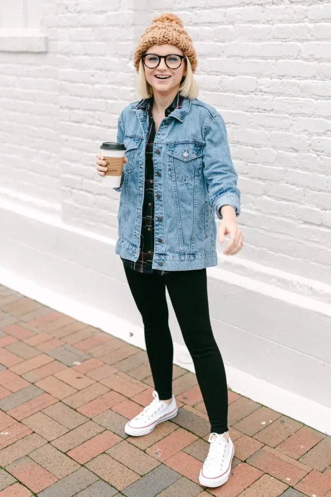 Light Wash Denim Jacket and Flannel Layers with Leggings, petite woman in open light wash denim jacket over dark plaid flannel, black leggings and white platform Converse with a camel pom beanie on a brick sidewalk.